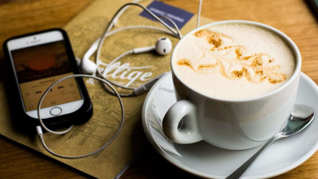 A phone with headphones playing a podcast influenced by AI technology, next to a cup of coffee