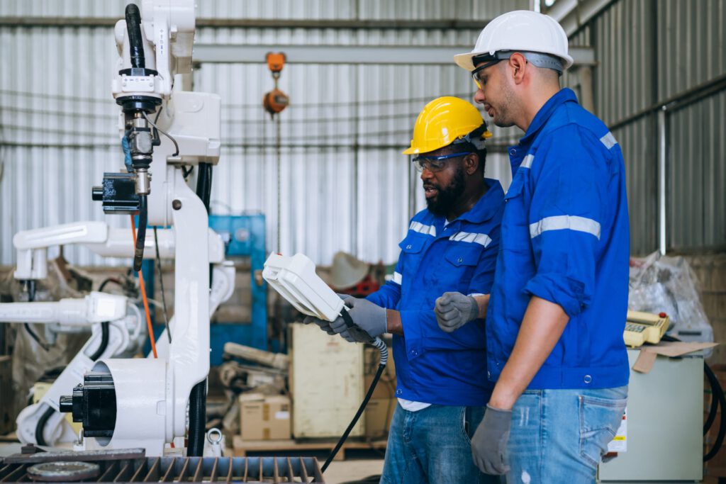 Engineer technician controlling robotic arms on computer laptop in an industrial setting