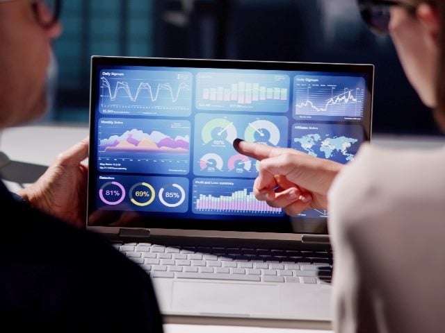 Two analysts look at a laptop screen showing data analytics in a piece about predictive analytics in CX.