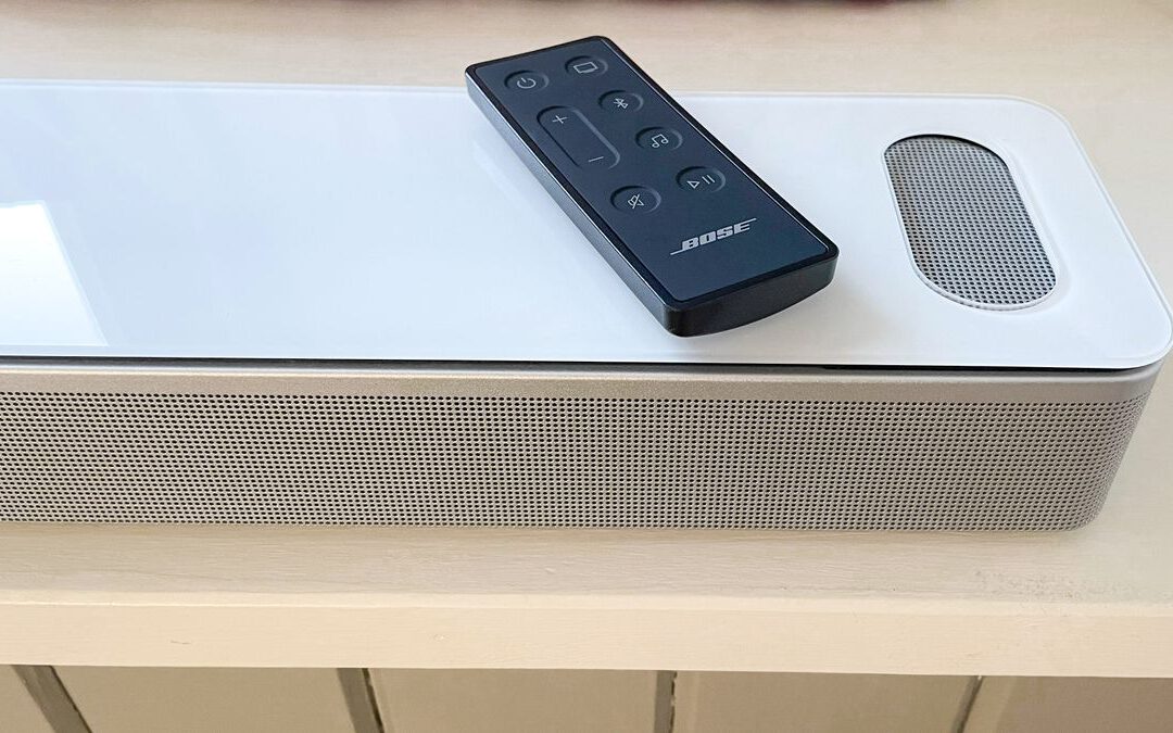 Bose Smart Ultra Soundbar in white with remote control placed on a window seat